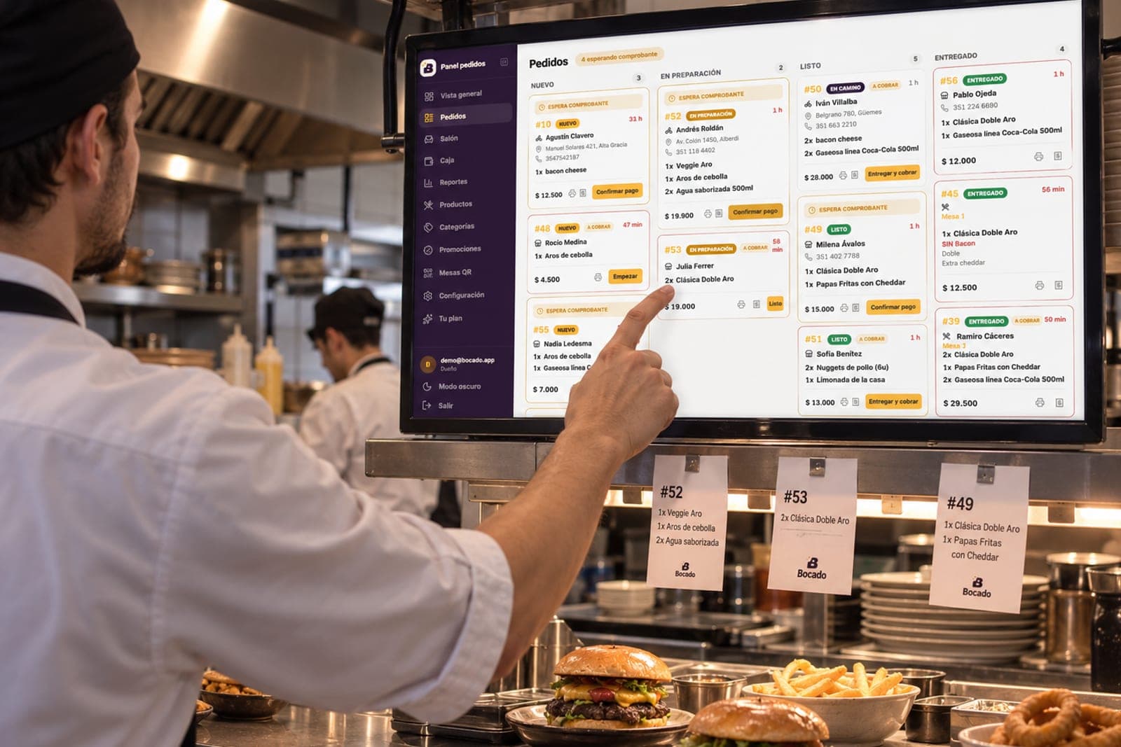 El tablero de pedidos de Bocado en una pantalla colgada en la cocina, con las comandas impresas debajo.
